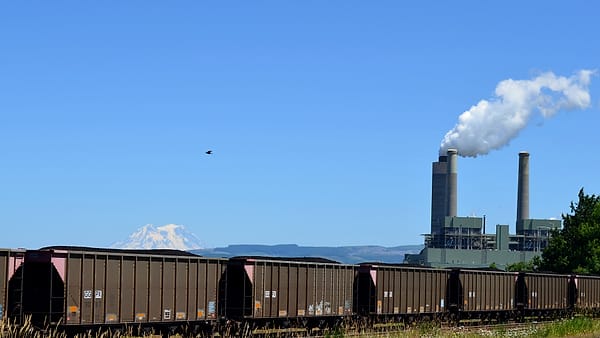 A conveyor belt carrying dark coal toward a tall storage silo under a flat gray sky