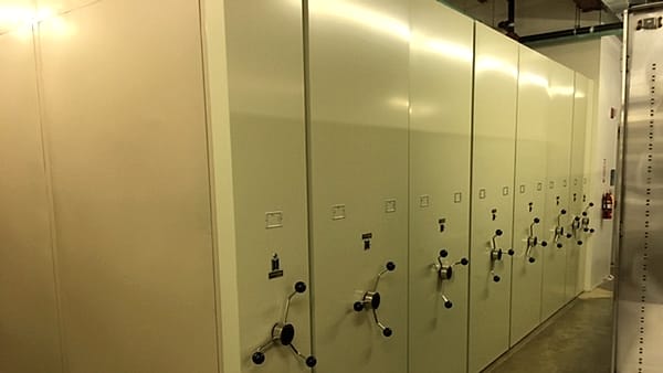 Numbered folders arranged in sequence on a long table, with a ruled index sheet and a pencil at one end.