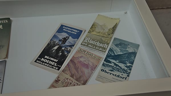 A stapled paper booklet lying open on a plain desk with a window reflected faintly on the page