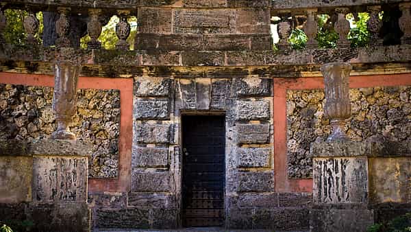 A closed steel gate with a heavy padlock set into a stone wall, photographed straight on in flat light