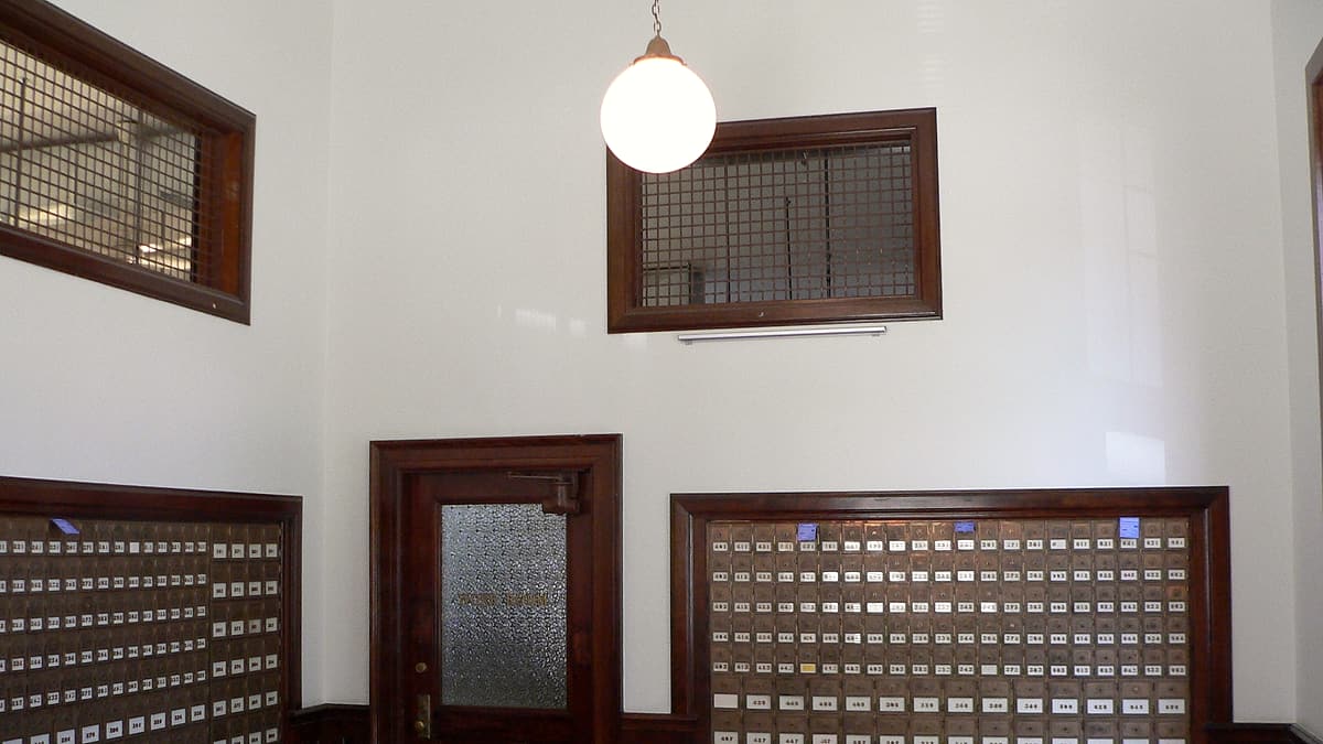 An empty wooden hearing room with a raised bench, microphones on stands and rows of vacant public seating.