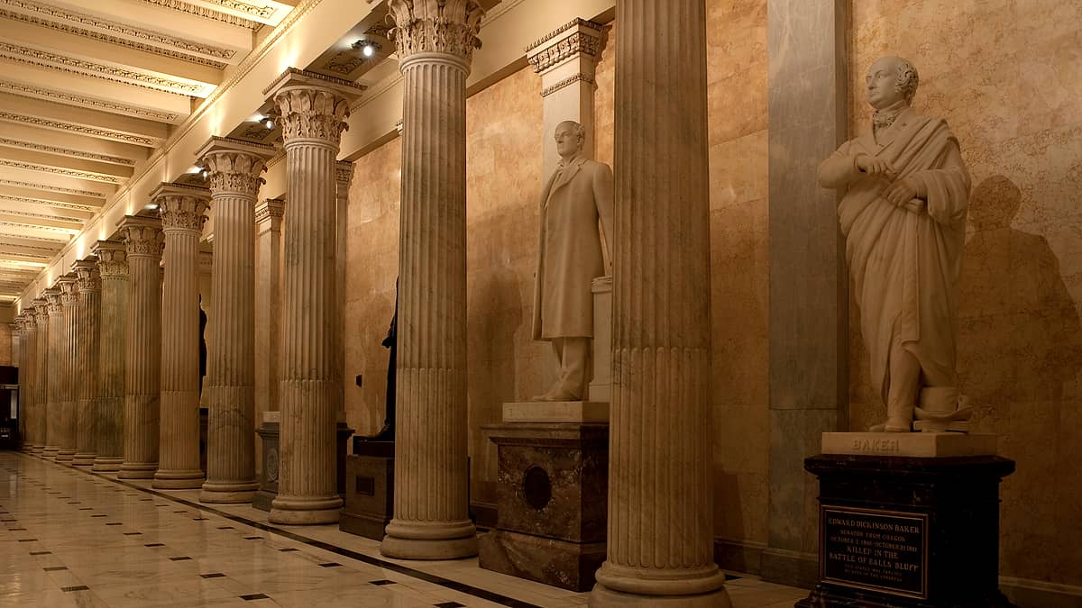 A long marble corridor with tall arched windows and a polished stone floor reflecting the daylight from outside.